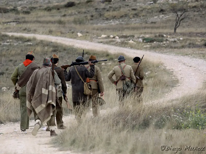 Columna de recreadores de GRH El Comité, con uniformes de la Guerra Civil Española y fusiles, marchando por un camino polvoriento durante una recreación histórica en las ruinas de Belchite.