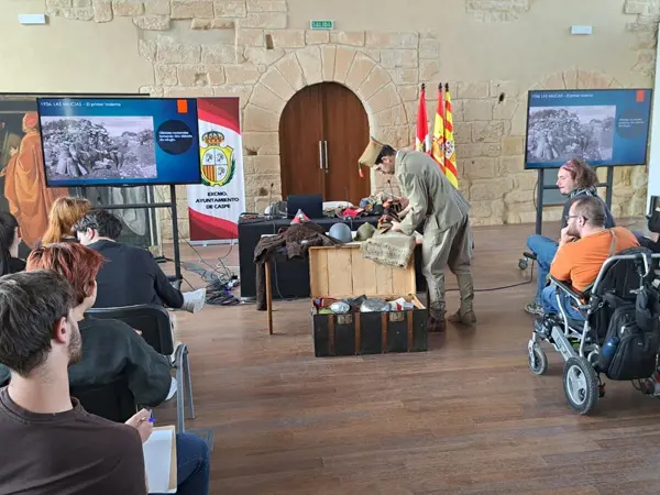 Miembro de GRH El Comité impartiendo una charla de divulgación histórica sobre la Guerra Civil Española, señalando y manipulando equipo y réplicas militares mientras el público observa.