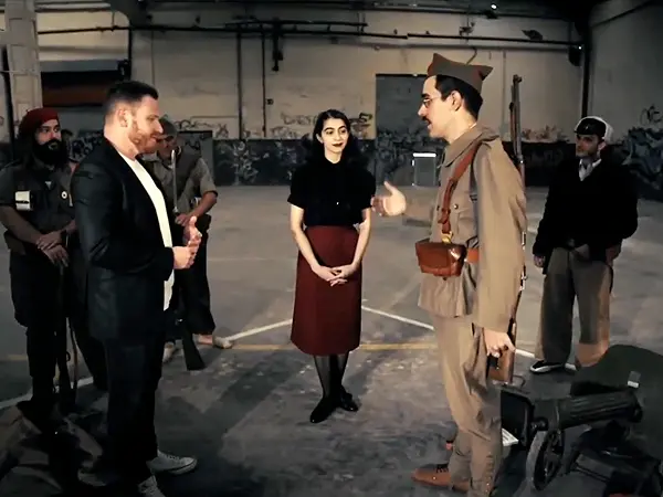 Un miembro de GRH El Comité, vestido con uniforme de época de la Guerra Civil Española, es entrevistado por un presentador de Antena Aragón durante la grabación de un programa, rodeado de otros recreadores y material histórico.