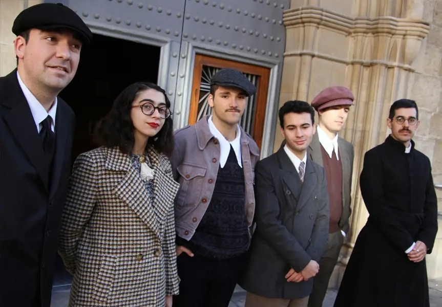 Grupo de recreadores con vestimenta civil de los años 30, junto a un sacerdote, posando en la puerta de una iglesia durante la recreación histórica en Flix.